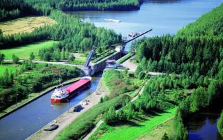 Suuri rahtialus Saimaan kanavassa. Ilmakuva, jossa kesäistä maisemaa.