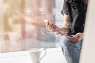 Henkilö istuu kädessään puhelin ja tablettitietokone