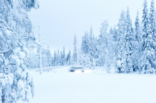 Talvinen maisemakuva, jossa auto ajaa lumisella tiellä.
